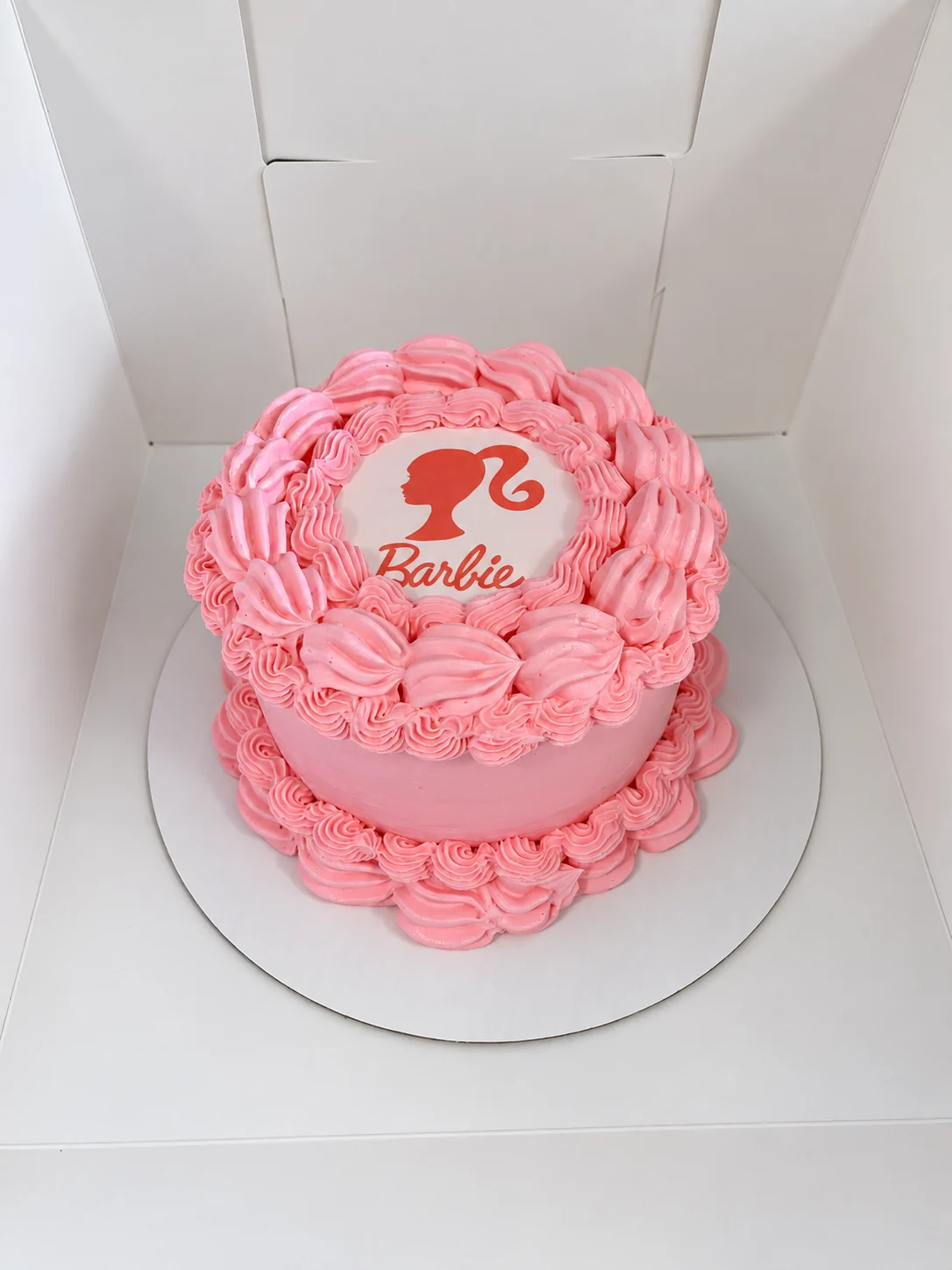 Round pink cake with vintage-style piping and a red Barbie silhouette and wordmark