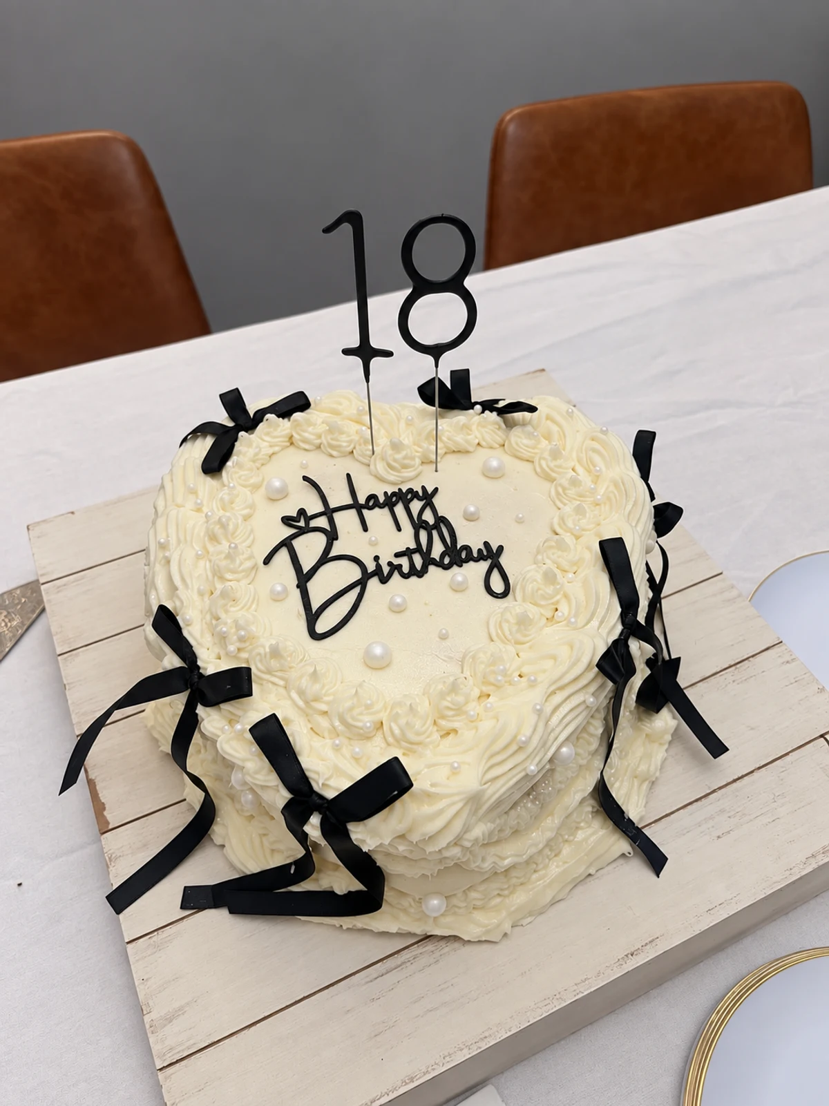 Cream birthday cake with black ribbon bows, piped frosting, and an 18 topper