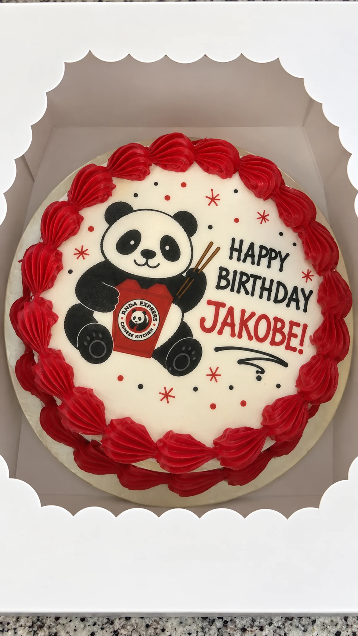 Round birthday cake with a Panda Express theme and red piped border inside a bakery box