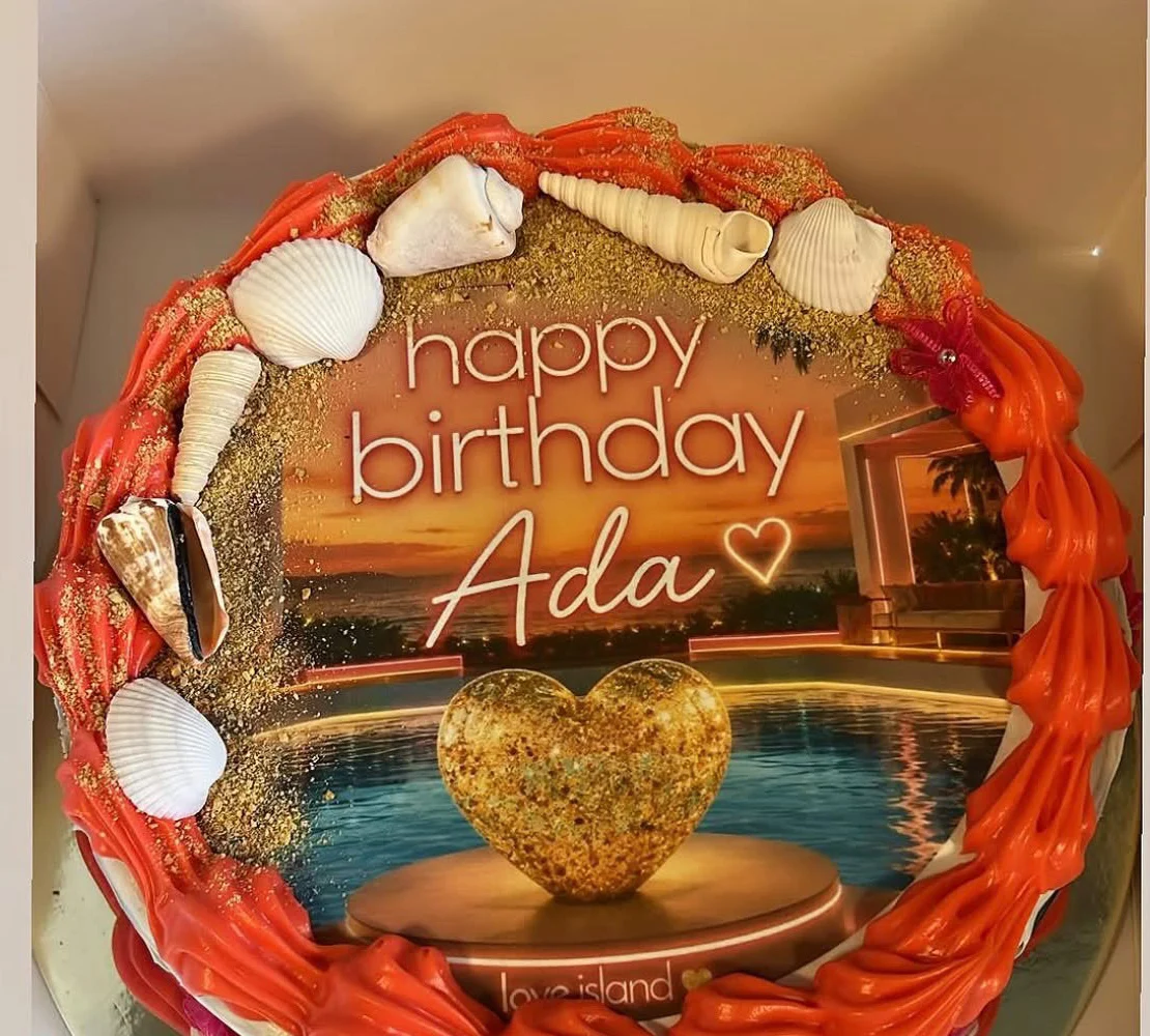 Personalized birthday cake featuring a beach scene with orange and white piping and a gold heart