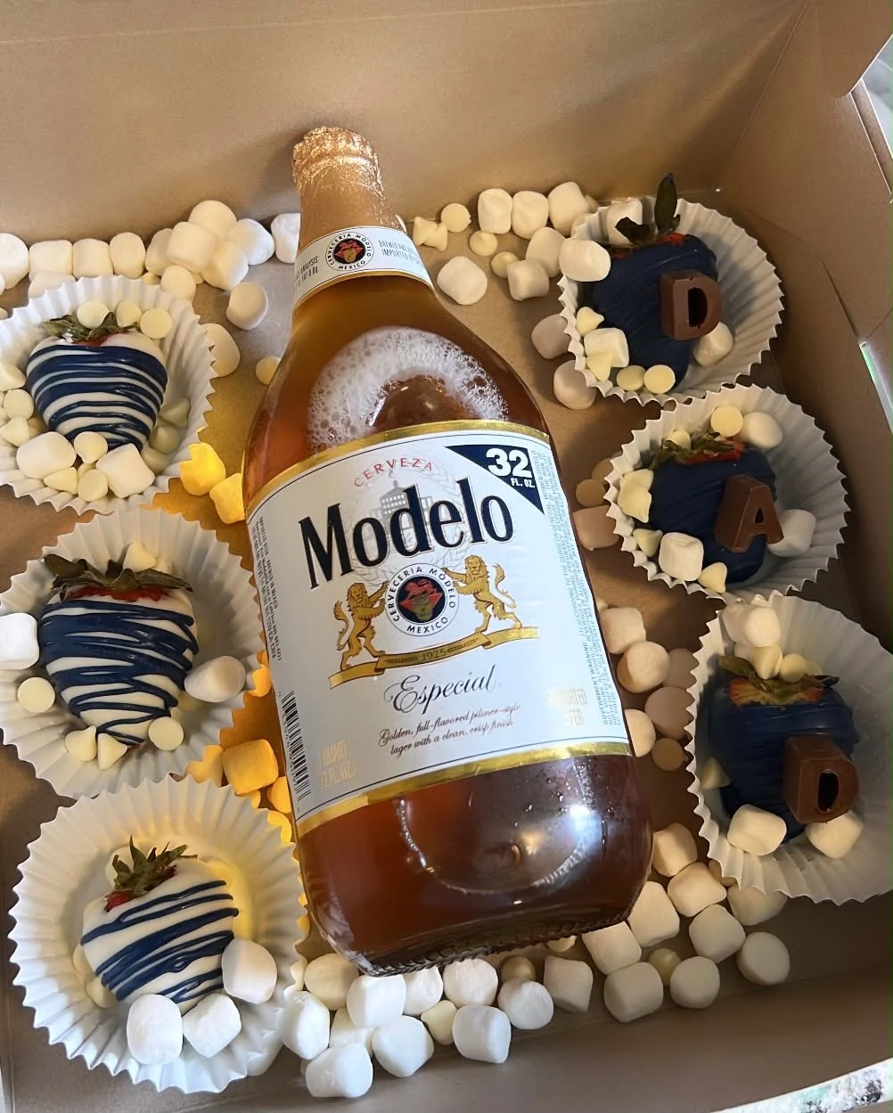 Gift box with decorated chocolate-covered strawberries, lettered treats, marshmallows, and a Modelo bottle